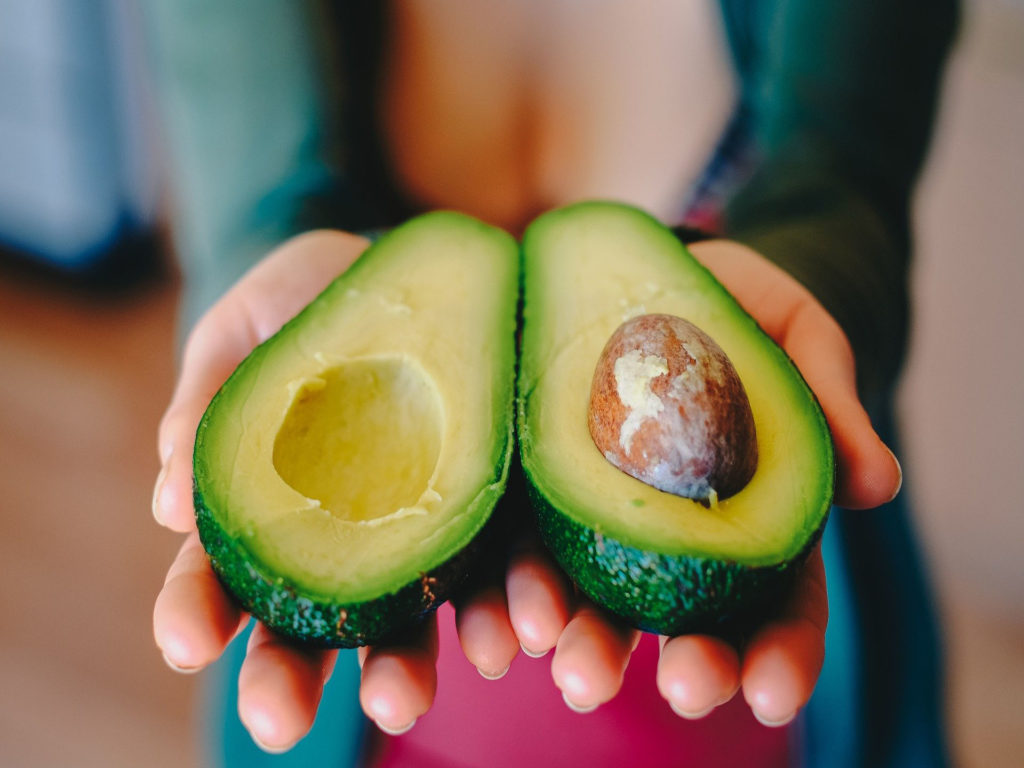 Close-up image of an avocado cut in half held by hands.