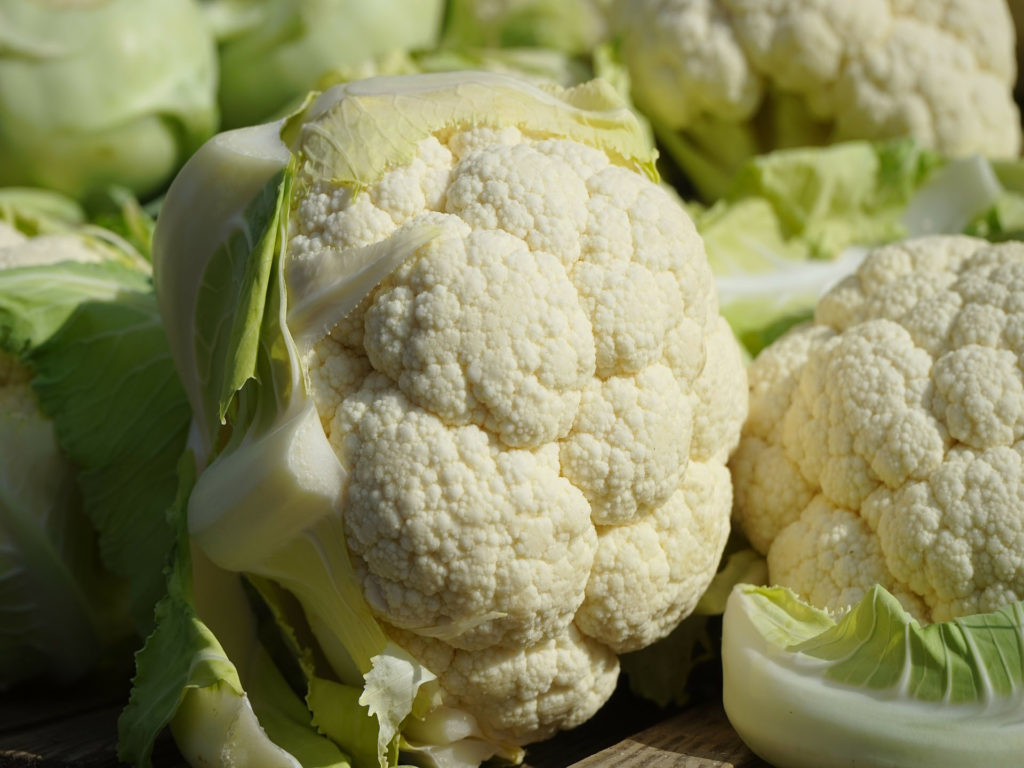 Close-up photo of cauliflower heads with leaves.