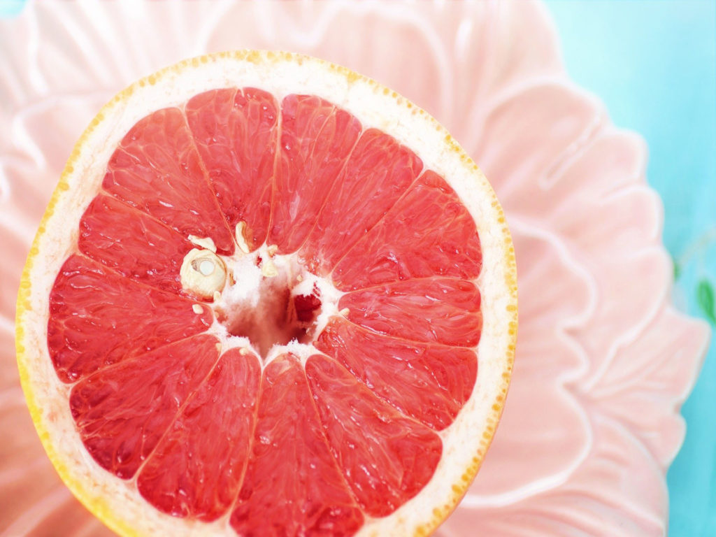 Close-up photo of a grapefruit half on a pink flower plate.